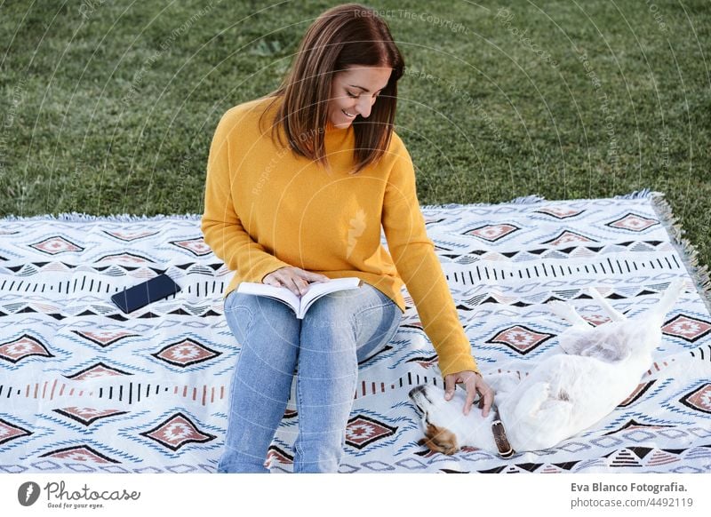 Frau hat Spaß mit Jack-Russell-Hund im Park, sitzt auf einer Decke während der Herbstzeit. Frau liest ein Buch und kuschelt mit Hund. Haustiere und Liebe Konzept