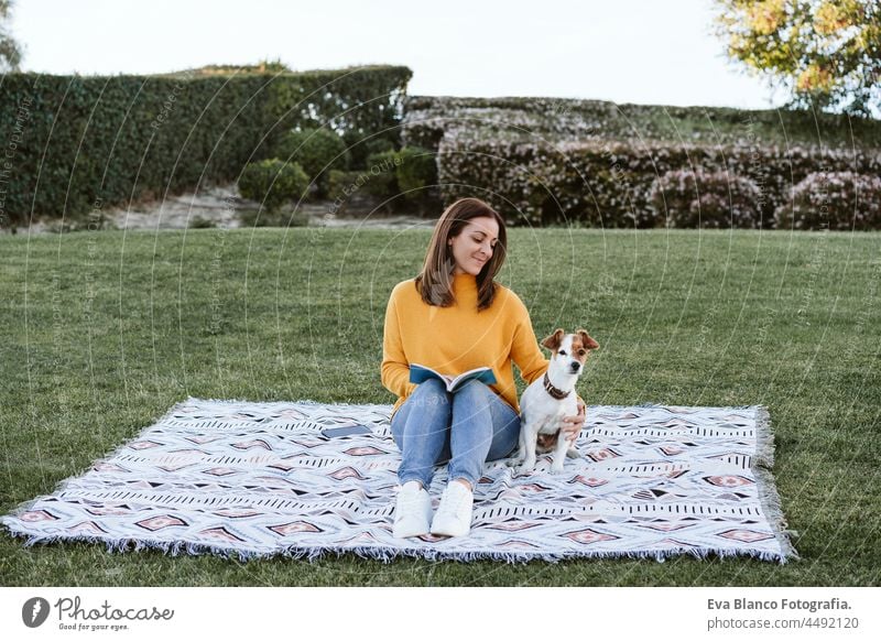 glückliche Frau, die Spaß mit Jack-Russell-Hund im Park hat, sitzt auf einer Decke während der Herbstsaison. Frau, die ein Buch liest, während sie den Hund umarmt. Haustiere und Liebe Konzept