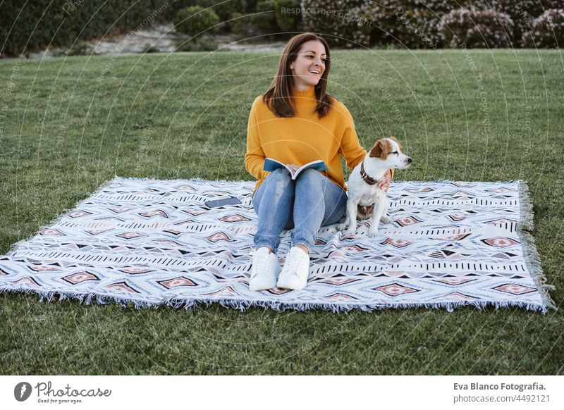 Frau, die Spaß mit Jack Russell Hund im Park, sitzen auf der Decke im Herbst Saison. Frau, die ein Buch liest, während sie ihren Hund umarmt. Haustiere und Liebe Konzept