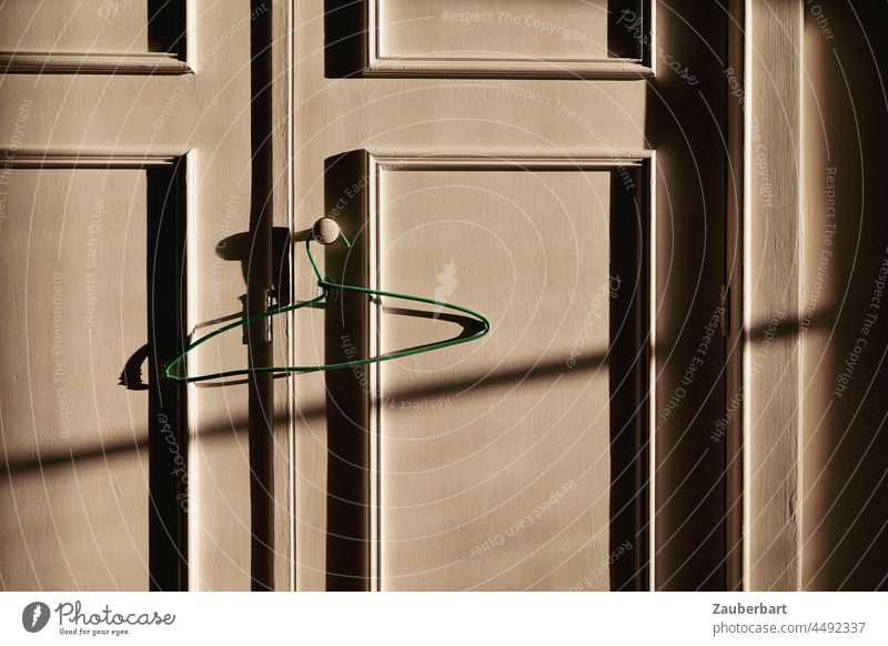Türen eines Kleiderschranks mit grünem Kleiderbügel im Seitenlicht mit Schattenwurf Bügel Schrank Schranktür Aufleistung Profilleisten Drahtbügel hängen