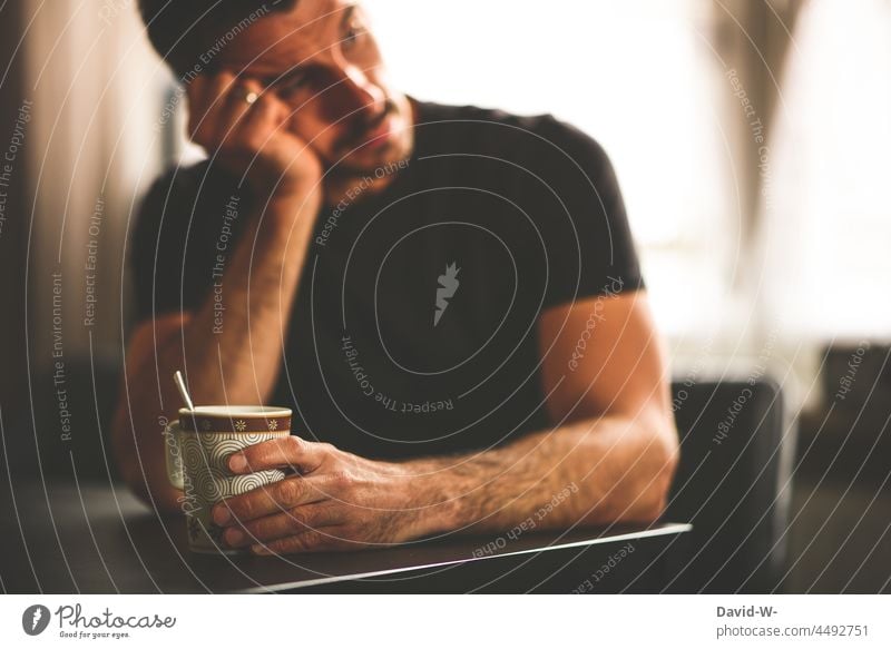 nachdenklicher Mann sitzt am Tisch und hält einen Kaffeebecher in der Hand denken Gedanken Zukunftsangst Zweifel Erschöpfung Kaffeepause gedankenverloren sitzen