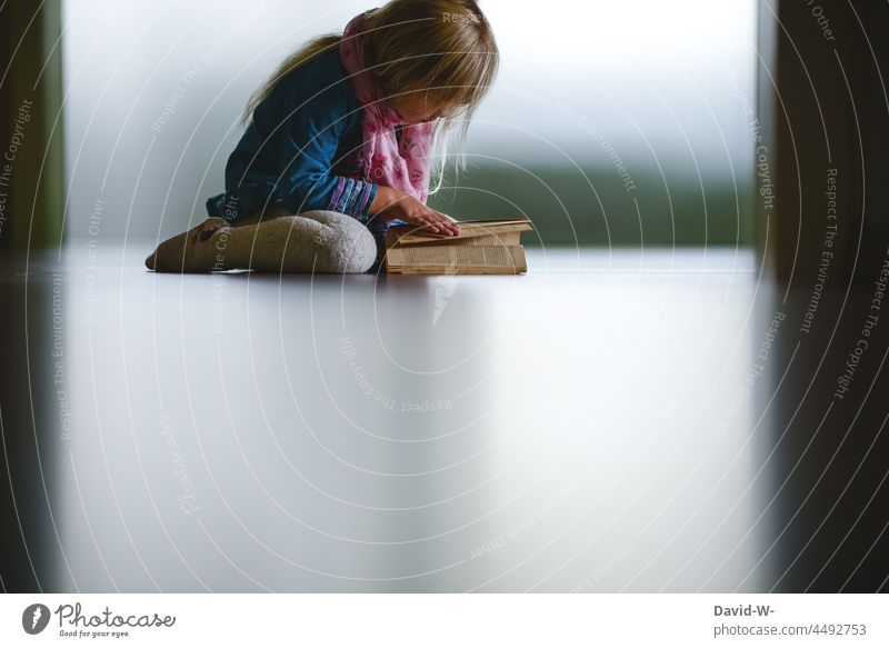 Kind sitzt auf dem Boden und blättert in einem Buch wissbegierig lesen blättern interessiert jung hochbegabt lernen Wissen klug schlau Kindheit Buchseite