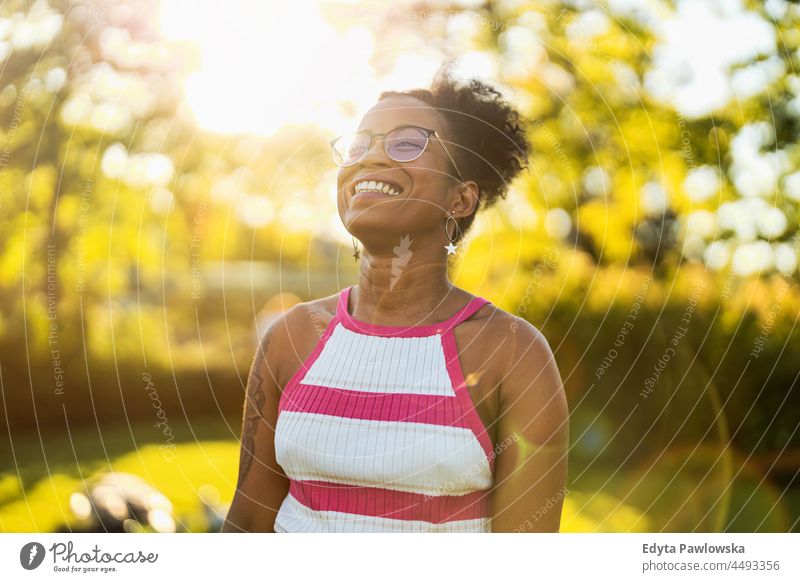 Porträt einer jungen Frau, die bei Sonnenuntergang im Freien lächelt Jahrtausende Brille lockig Freude außerhalb farbenfroh Afro-Look selbstbewusst Schönheit
