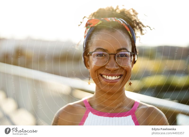 Porträt einer jungen Frau, die bei Sonnenuntergang im Freien lächelt Jahrtausende Brille lockig Freude außerhalb farbenfroh Afro-Look selbstbewusst Schönheit