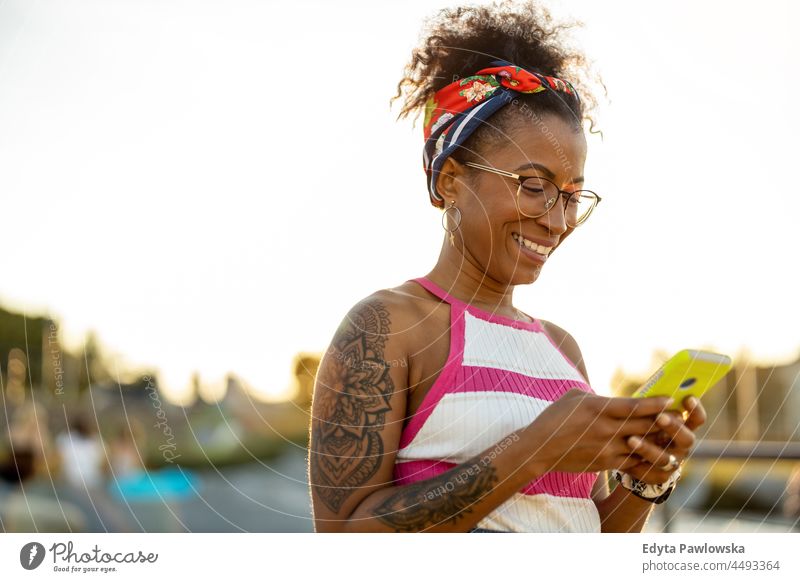 Junge Frau benutzt ein Mobiltelefon in der Stadt Jahrtausende Brille lockig Freude außerhalb farbenfroh Afro-Look selbstbewusst Schönheit Urlaub reisen