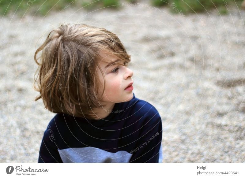 Porträt eines Jungen mit halblangen dunkelblonden Haaren, der zur Seite schaut Kind Mensch Schulkind Blick zur Seite Oberkörper draußen Gesicht Haare & Frisuren