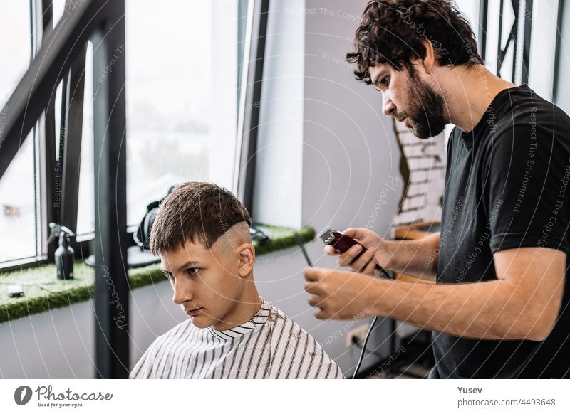 Stylischer Friseur schneidet einem jungen Mann die Haare. Professionelle Herrenrasur und Haarschnitt in einem Friseurladen oder Friseursalon. Haarpflege