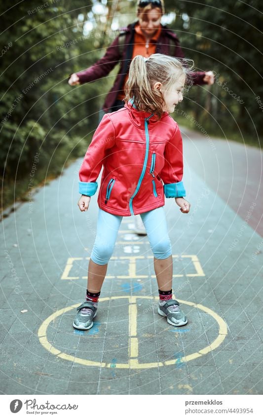 Aktives kleines Mädchen spielt Himmel und Hölle auf einem Spielplatz im Freien springend Spielen schwofen Vorschule Kind Spaß Kreide spielen außerhalb Übung