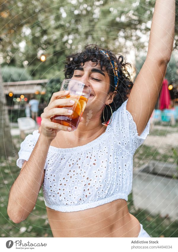 Unbekümmerte ethnische Frau trinkt Cocktail auf einer Party trinken Tanzen Sommer genießen feiern Glas Garten Getränk Lächeln heiter Wochenende positiv jung
