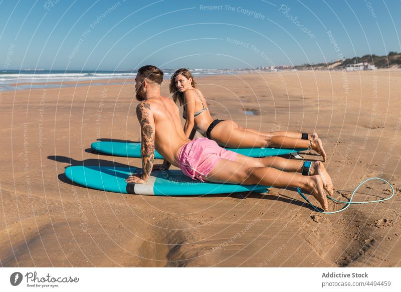 Sportliches Paar beim Aufwärmen auf Surfbrettern an der Küste Sportler Surfer Strand Hobby Dehnung vorbereiten Wassersport Seeküste Badebekleidung Frau Mann