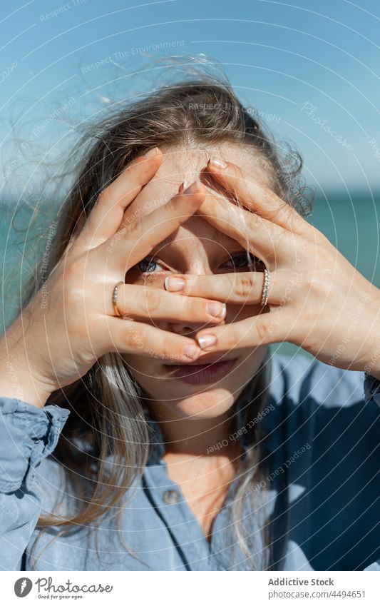 Frau schaut durch die Hände in die Kamera Sommer Sonnenlicht Küstenlinie Meeresufer Hand trendy tagsüber Wind Tierhaut friedlich Vorschein Zeitgenosse