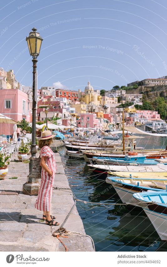 Frau steht am Ufer in der Nähe des Meeres in einer Küstenstadt Stauanlage Stadt Boot Maure Stil MEER Portwein procida Italien flegreische Inseln Hut Kleid