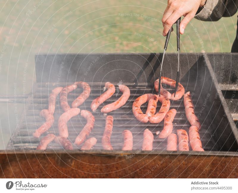Anonyme Person beim Braten von Würstchen auf dem Grill in freier Natur Wurstwaren Fleisch Grillrost Barbecue Holzkohle Landschaft Gitter grillen Lebensmittel