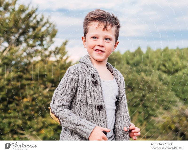 Süßer kleiner Junge lächelnd und wegschauend in der Natur Lächeln Berge u. Gebirge Strickjacke Wald Baum Landschaft Kind positiv Porträt Glück Kindheit wolkig