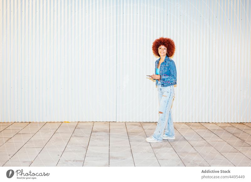 Stilvolle Frau mit Smartphone auf der Straße Browsen online Afro-Look Mode trendy Bekleidung Wand Surfen Textnachricht Funktelefon Apparatur Gerät Frisur
