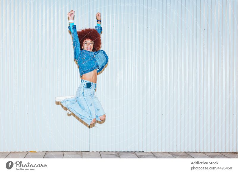 Glückliche Frau springt auf der Straße Afro-Look Stil Mode Bekleidung Wand Outfit Spaß haben sorgenfrei springen Aktivität aktiv Energie Arme hochgezogen