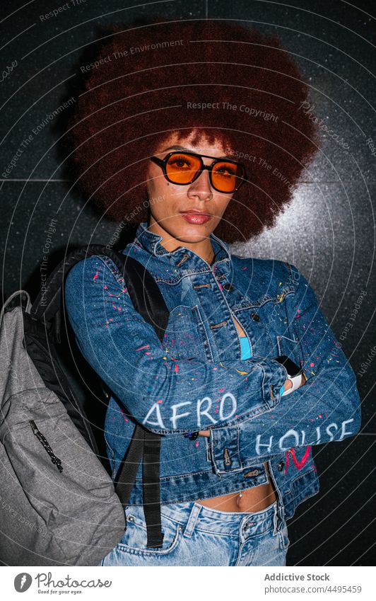 Seriöse Frau in stilvoller Kleidung auf dunkler Straße Jeansstoff Afro-Look Stil Mode Bekleidung Streetstyle Rucksack Abend anhaben dunkel Dämmerung Frisur