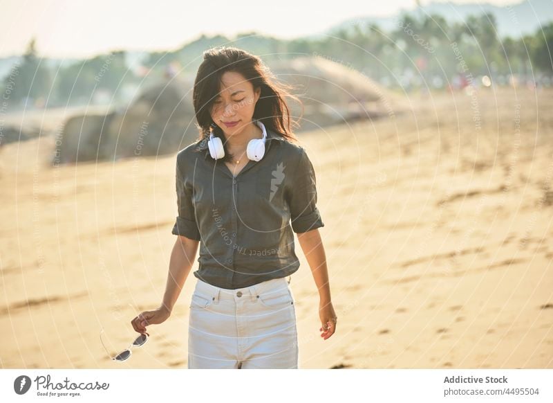 Nachdenkliche asiatische Frau beim Musikhören am Strand Seeküste Meeresufer Spaziergang Kopfhörer meloman Gesang Zeitvertreib zuhören schlendern nachdenklich