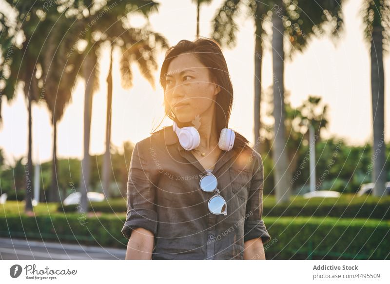 Asiatische Frau mit Kopfhörern auf der Straße meloman Stil Musik Hobby Stadt Zeitvertreib trendy Windstille ethnisch Schwarzes Haar attraktiv asiatisch Sommer