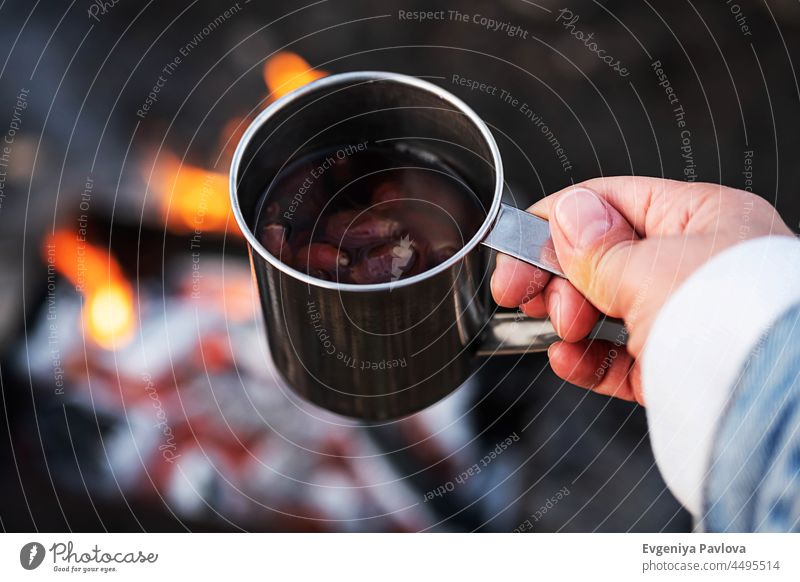 Frau Hand halten Hagebuttentee in Stahlbecher gegen Lagerfeuer. Umweltfreundlicher Tourismus, nachhaltiger Lebensstil. trinken heiß Tee Becher Tasse