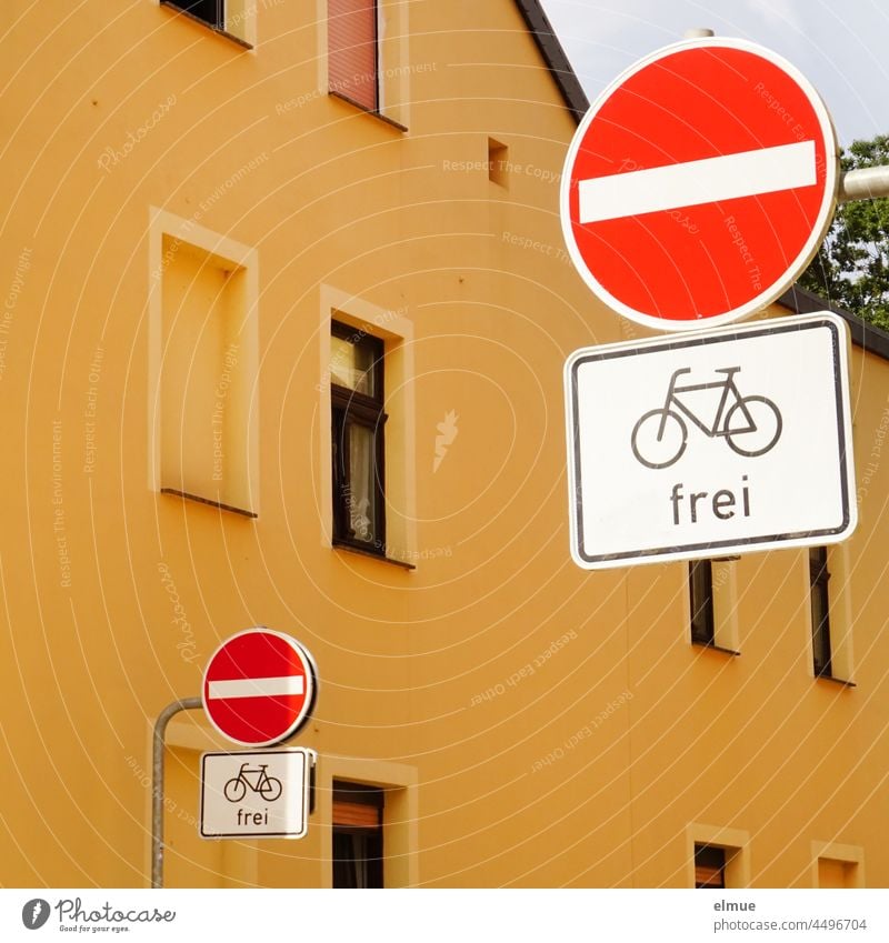 Schilder I Vor einem gelben Haus stehen auf der linken und rechten Straßenseite Verkehrszeichen - Verbot der Einfahrt - mit Zusatzschild - Radfahrer frei - / VZ 267 / VZ 1022-10 / Einbahnstraße