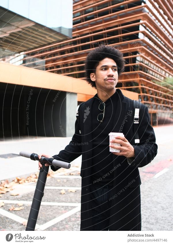Trendiger ethnischer Typ mit Roller, der auf der Straße Kaffee zum Mitnehmen trinkt Mann Tretroller Stil selbstsicher Imbissbude elegant afroamerikanischer Mann