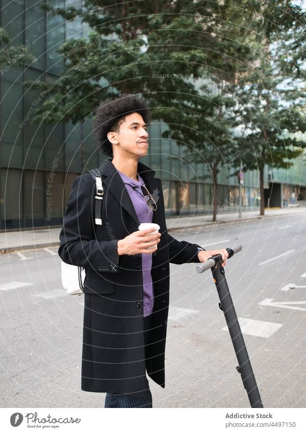 Trendiger ethnischer Typ mit Roller, der auf der Straße Kaffee zum Mitnehmen trinkt Mann Tretroller Stil selbstsicher Spaziergang Imbissbude elegant