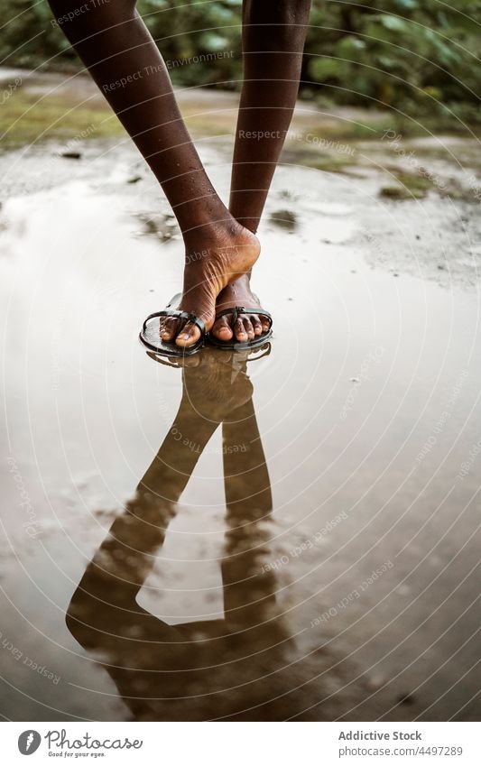 Schwarzes barfüßiges Kind steht in einer Pfütze auf der Straße Barfuß nass Asphalt Wasser Bürgersteig Flip-Flop Sandale São Tomé und Príncipe Afrika Afrikanisch
