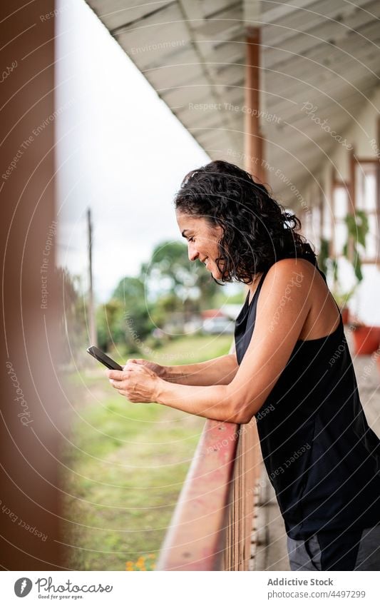 Lächelnde ethnische Frau benutzt ihr Smartphone auf einer Terrasse in einem Dorf benutzend Glück Landschaft Nachricht Kommunizieren online Natur