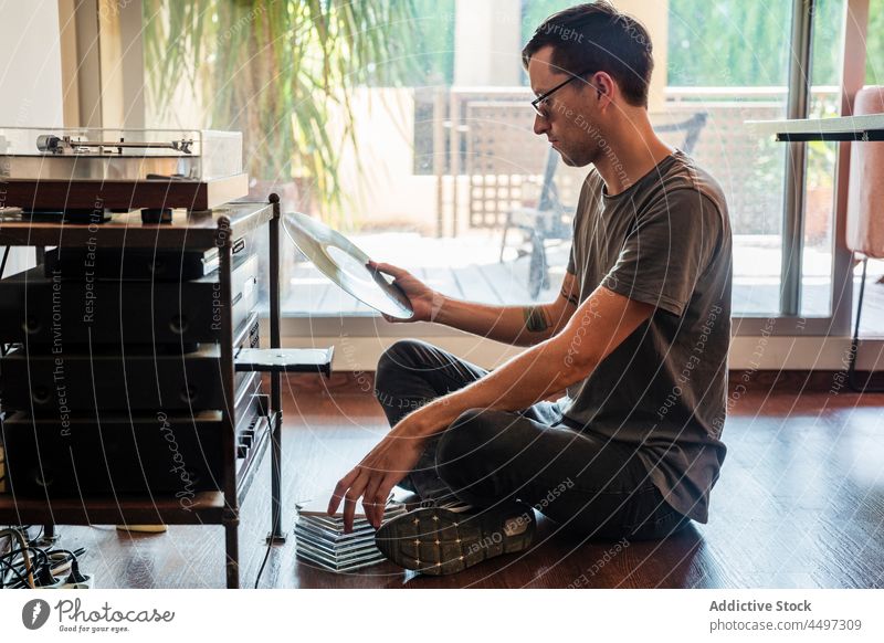 Ein Mann schaut sich eine Schallplatte an, während er in der Nähe des Players sitzt Spieler Aufzeichnen Vinyl Plattenteller Stock Musik Konzentration Nostalgie