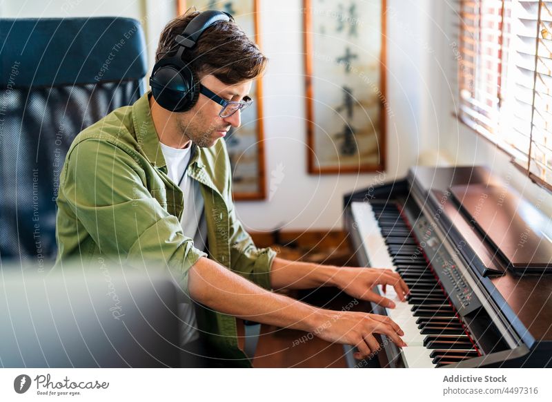 Männlicher Musiker spielt auf dem Klavier in einem hellen Raum Mann Pianist spielen Kopfhörer komponieren Instrument Melodie üben Talent männlich Fenster sitzen