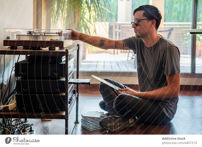 Ein Mann schaut sich eine Schallplatte an, während er in der Nähe des Players sitzt Spieler Aufzeichnen Vinyl Plattenteller Stock Musik Konzentration Nostalgie