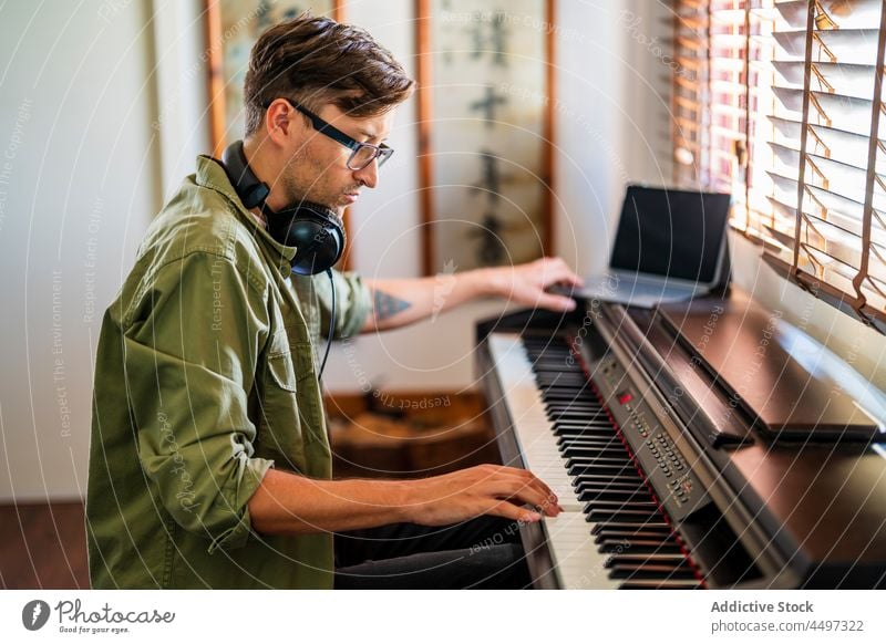 Männlicher Musiker spielt auf dem Klavier in einem hellen Raum Mann Pianist spielen Kopfhörer komponieren Instrument Melodie üben Talent männlich Fenster sitzen