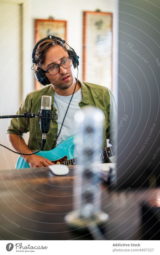 Gitarrist hält sein Instrument und benutzt einen Computer im Studio Mann Gitarrenspieler Kopfhörer Musiker Atelier Mikrofon Melodie Talent männlich Aufzeichnen
