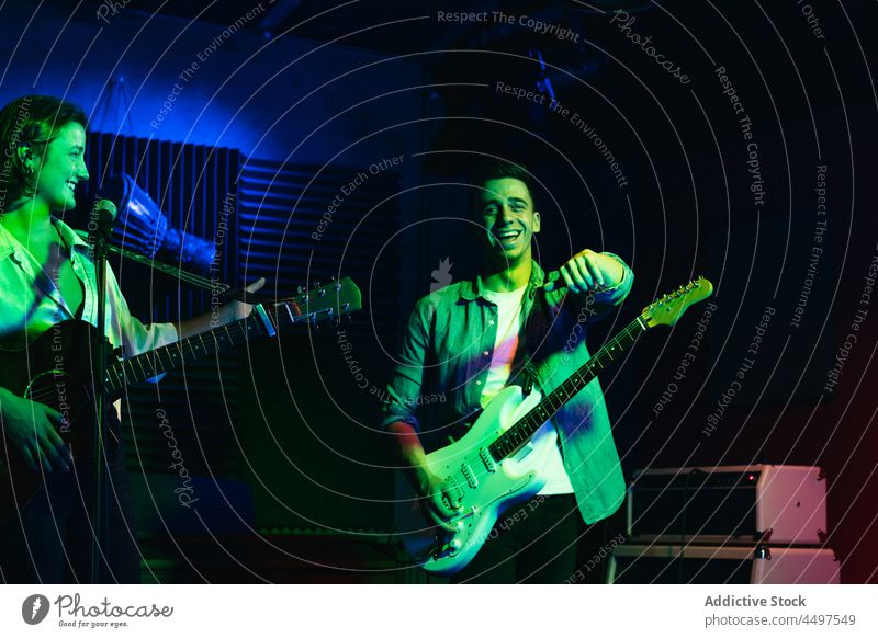 Lächelnde Musiker spielen Gitarre und singen in einem Club Menschengruppe Band Instrument Mikrofon ausführen neonfarbig jung positiv Gitarrenspieler Nachtclub