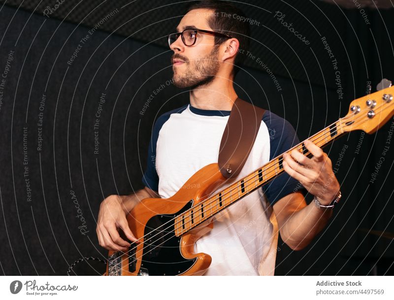 Männlicher Musiker spielt Bassgitarre im Studio Mann Gitarre spielen Instrument Club ausführen Hobby Talent Veranstaltung männlich jung lässig Brille Licht