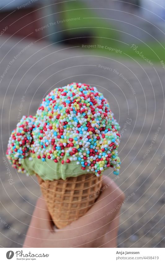 Eiscreme mit bunten Zuckerstreuseln in der Hand als Nahaufnahme Speiseeis Lebensmittel süß Farbe farbenfroh geschmackvoll kalt Hintergrund grau verschwommen