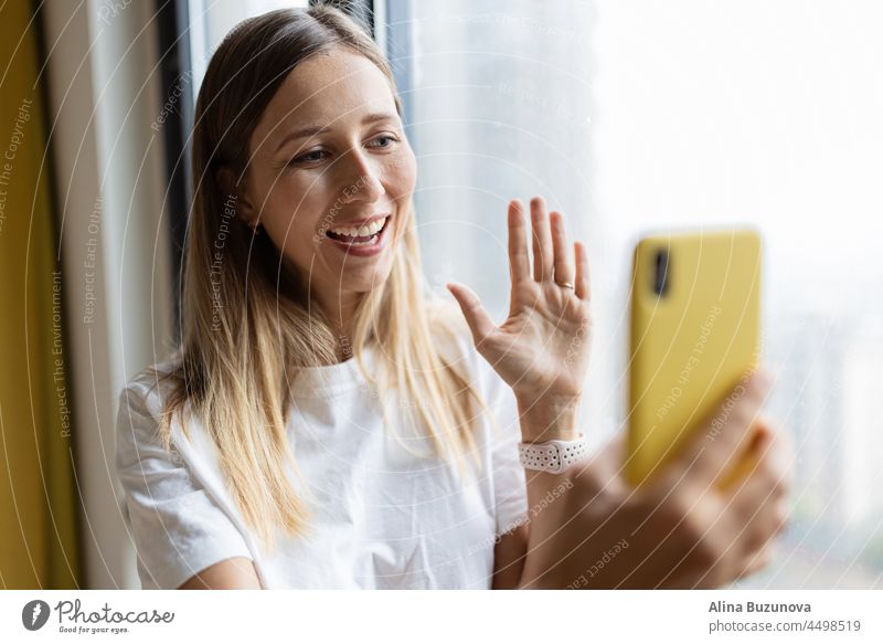Junge hübsche Millennial-Frau hält Handy zu Hause oder in einem Café in der Nähe des Fensters. Video-Chat Lebensmittel-Lieferung Online-Shopping