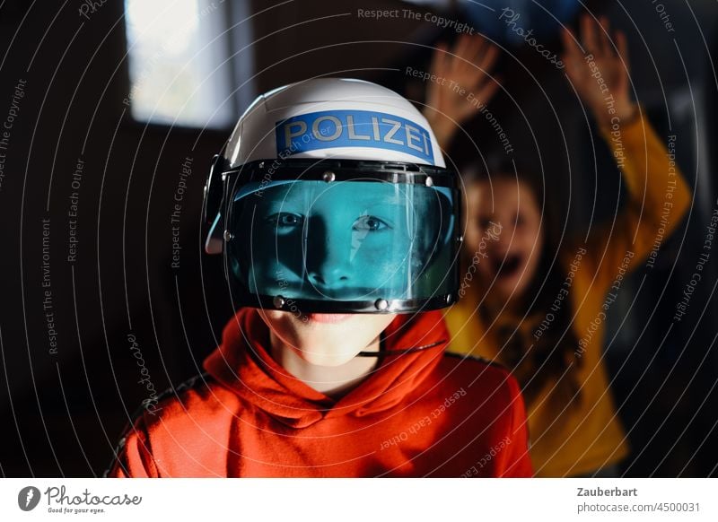 Junge mit Polizeihelme und blauem Visier, dahinter ein Mädchen erschrecken Spiel Kinder Kindheit Spaß spielen Freizeit rot gelb Freude verkleiden Verkleidung