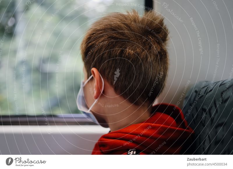 Junge mit Maske und rotem Hoodie schaut aus dem Fenster der S-Bahn Mundschutz Covid grün Pandemie Corona SPNV Nahverkehr schauen Kind Kindheit Infektionsgefahr