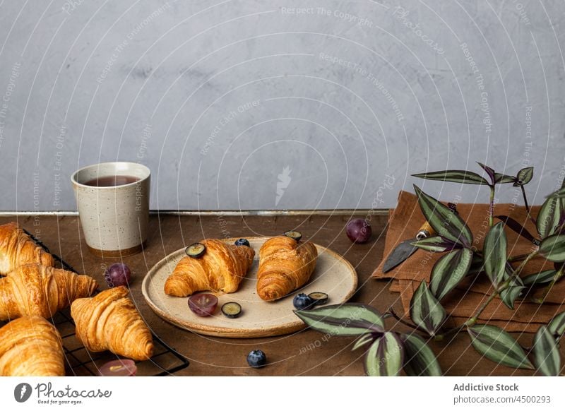 Leckere Croissants stehen neben einer Tasse Tee auf einem Holztisch Dessert Frühstück Morgen lecker geschmackvoll gebacken Frucht Lebensmittel Teller süß frisch