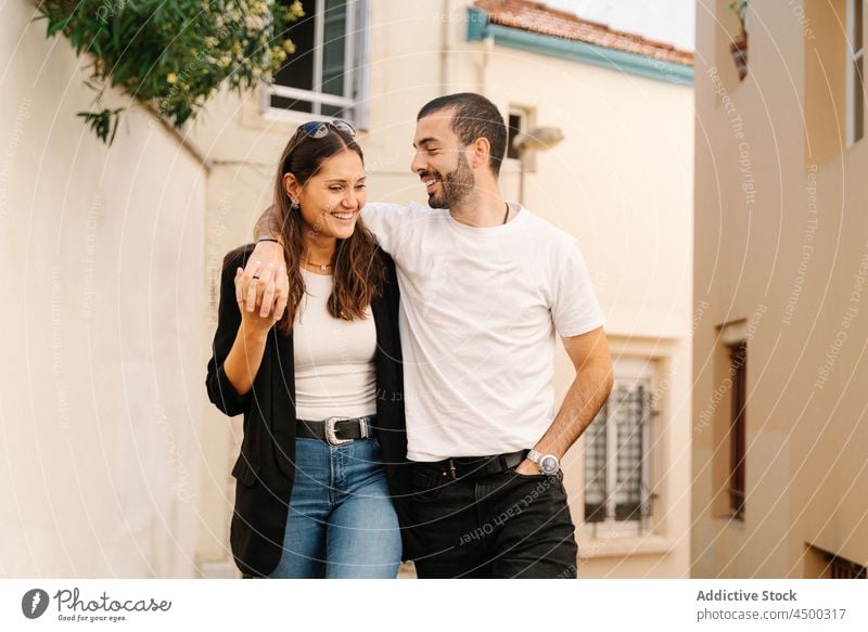 Glückliches junges ethnisches Paar, das sich kuschelt und auf der Straße spazieren geht kuscheln Spaziergang Lächeln romantisch Termin & Datum Partnerschaft