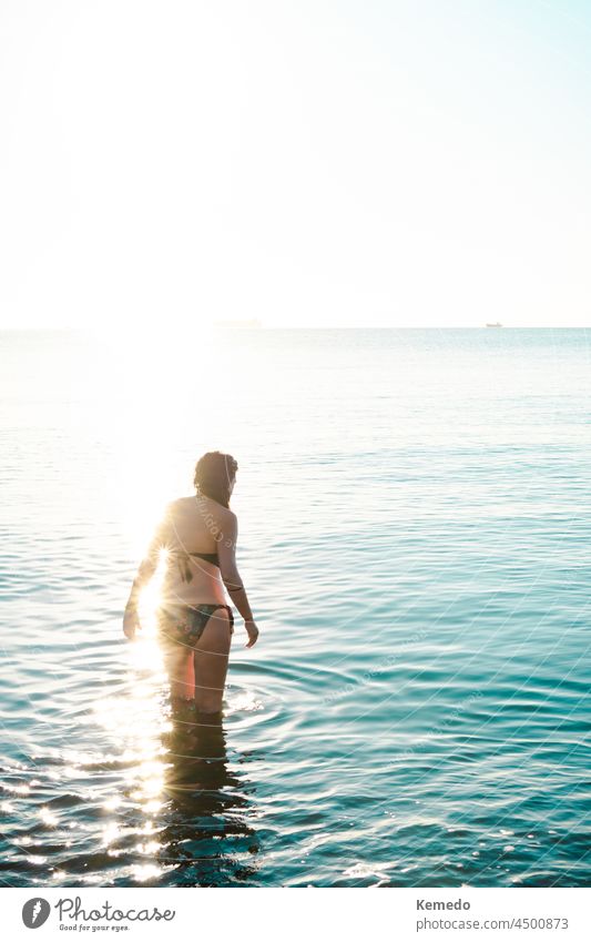 Frau, die bei Sonnenaufgang bei schönem Licht ins Meer geht, um zu schwimmen. Morgendämmerung MEER Strand Hintergrund Textfreiraum jung früh Wasser betreten Bad