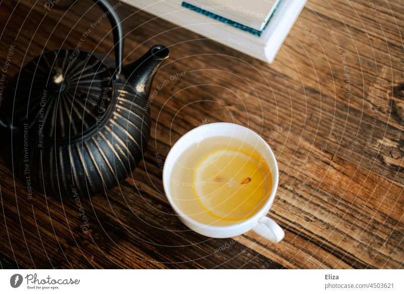 Teetasse mit Tee und Zitronenscheibe neben einer Teekanne auf Holztisch Heißgetränk Tasse Tisch Couchtisch Zitronentee warm gesund