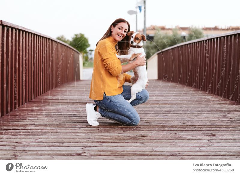 glückliche kaukasische Frau, die Spaß mit Jack Russell Hund im Park, Frau und Haustier stehen auf hölzernen Brücke im Herbst Saison. Haustiere und Liebe Konzept