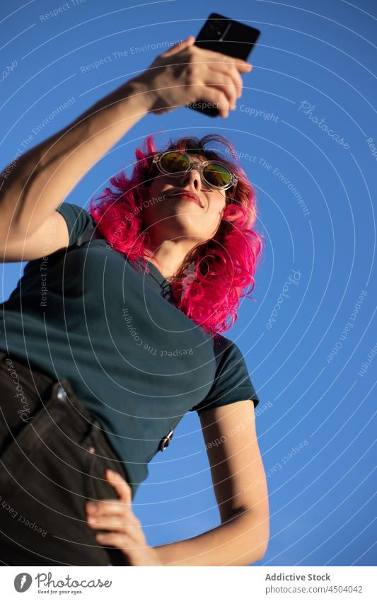 Stilvolle Frau surft auf ihrem Smartphone gegen den Himmel Browsen Straße Blauer Himmel Internet online rosa Haare Textnachricht Surfen Sonnenlicht Funktelefon