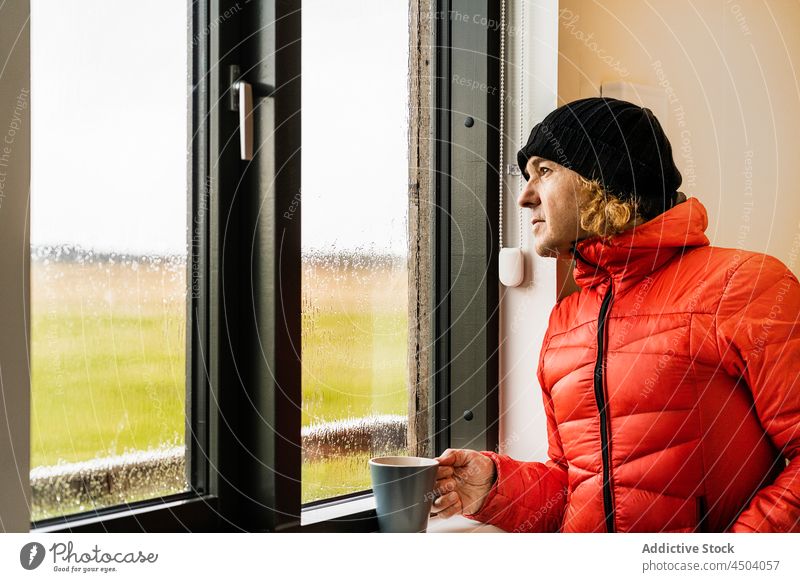 Verträumter Mann steht am Fenster in der Küche und trinkt Kaffee trinken verträumt Reisender Landschaft Heißgetränk Erholung Getränk Frühstück Regen männlich