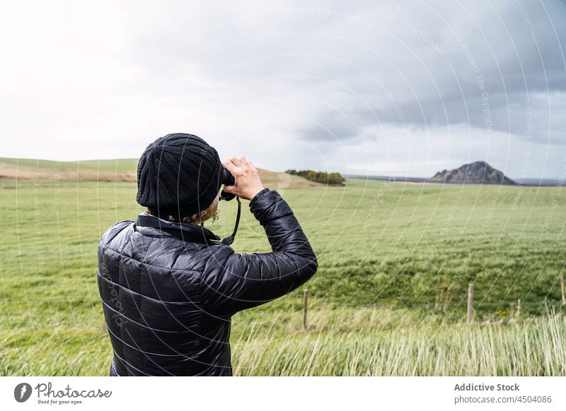 Anonymer männlicher Reisender, der mit einer Fotokamera auf einer Wiese stehend die Natur fotografiert Mann fotografieren Berge u. Gebirge Fotoapparat erkunden