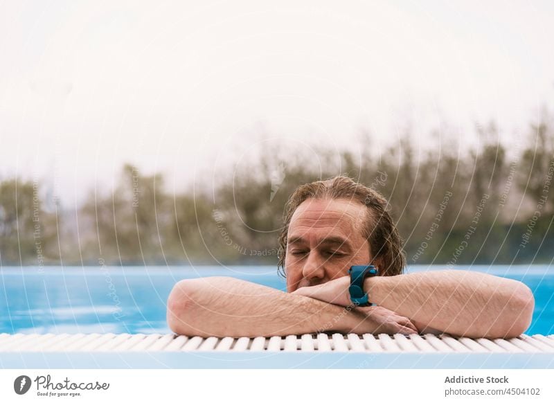 Mann mit lockigem Haar schwimmt in heißem Pool in der Natur Wasser Windstille ohne Hemd Augen geschlossen schwimmen besinnlich Flora nackter Torso männlich