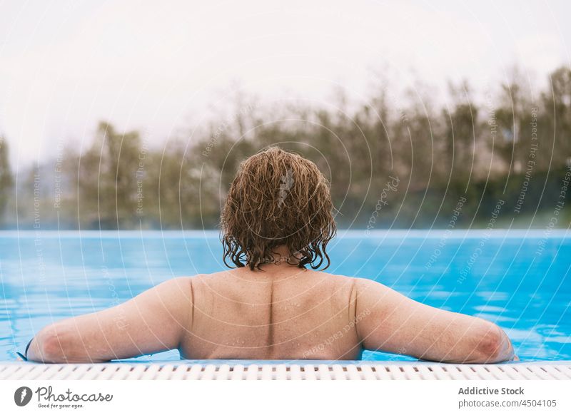 Anonymer Mann mit lockigem Haar schwimmt in einem heißen Pool in der Natur Wasser Windstille ohne Hemd sich[Akk] entspannen schwimmen besinnlich Flora